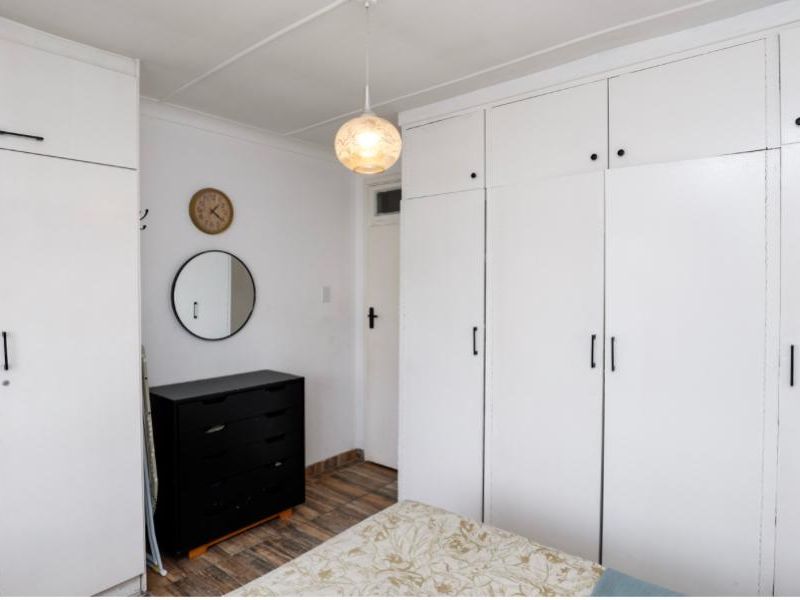 A bedroom featuring extensive white built-in cupboards, tiled flooring, and a central pendant light fixture.