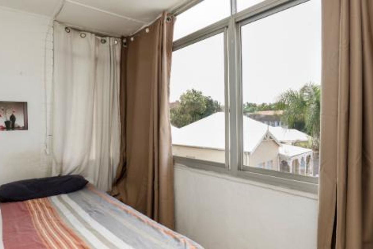 A compact bedroom featuring large aluminium-framed windows that provide natural light and views of the surrounding neighbourhood.