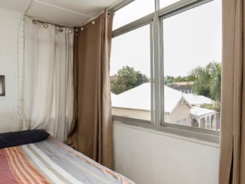 A compact bedroom featuring large aluminium-framed windows that provide natural light and views of the surrounding neighbourhood.