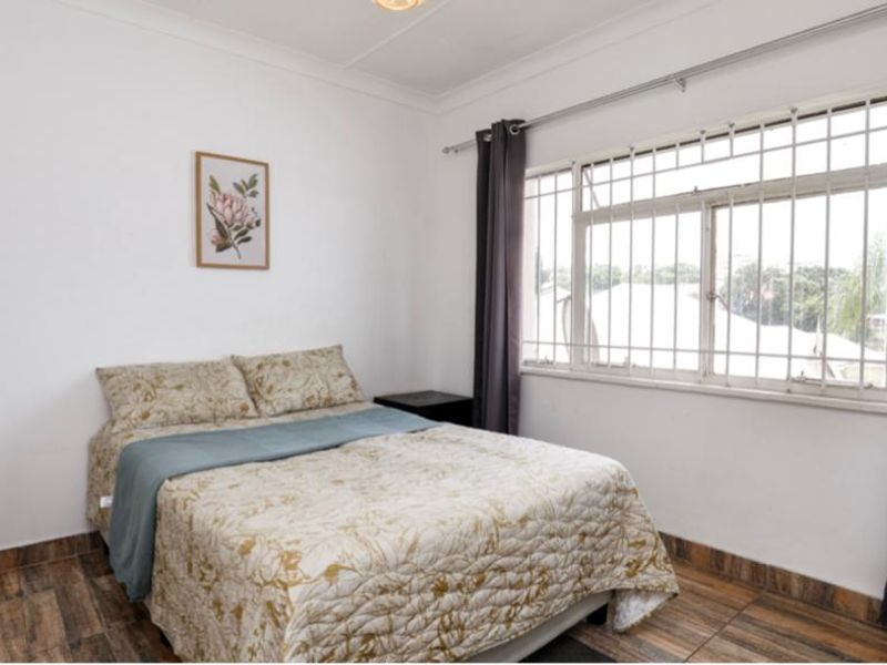 A functional bedroom featuring tiled flooring, a built-in wardrobe, and a window fitted with security bars.