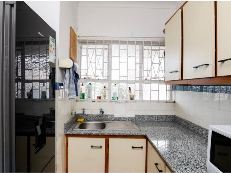 A functional kitchen featuring granite countertops, built-in cabinetry, and a stainless steel sink, with security bars installed on the window.