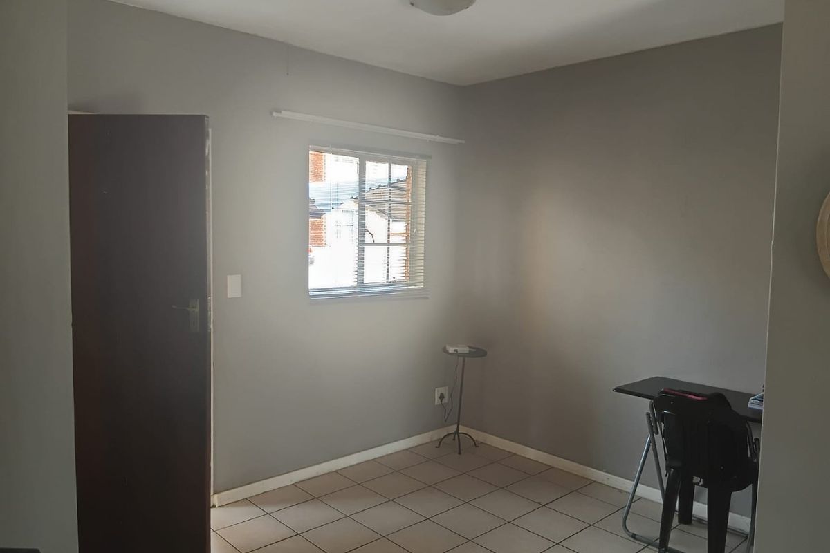 A simple, neutral-toned bedroom featuring tiled flooring and a window with fitted blinds, offering a clean and functional space.
