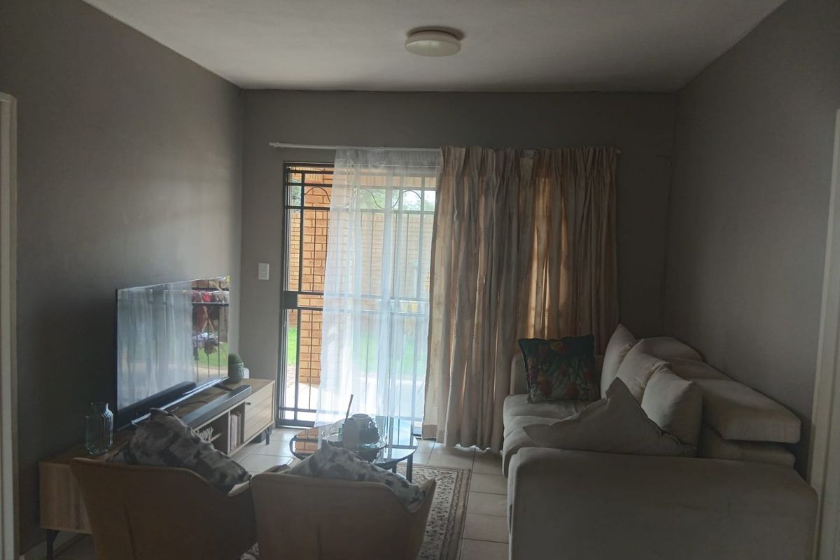 A living room featuring tiled flooring and a sliding glass door with an integrated security gate, providing access to the outdoor area.