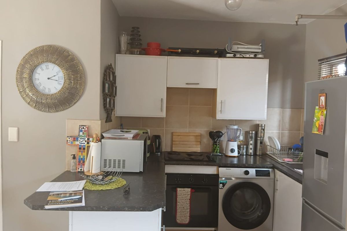 Compact kitchen featuring white cabinetry, dark laminate countertops, tiled backsplash, built-in oven, hob, and an integrated washing machine.