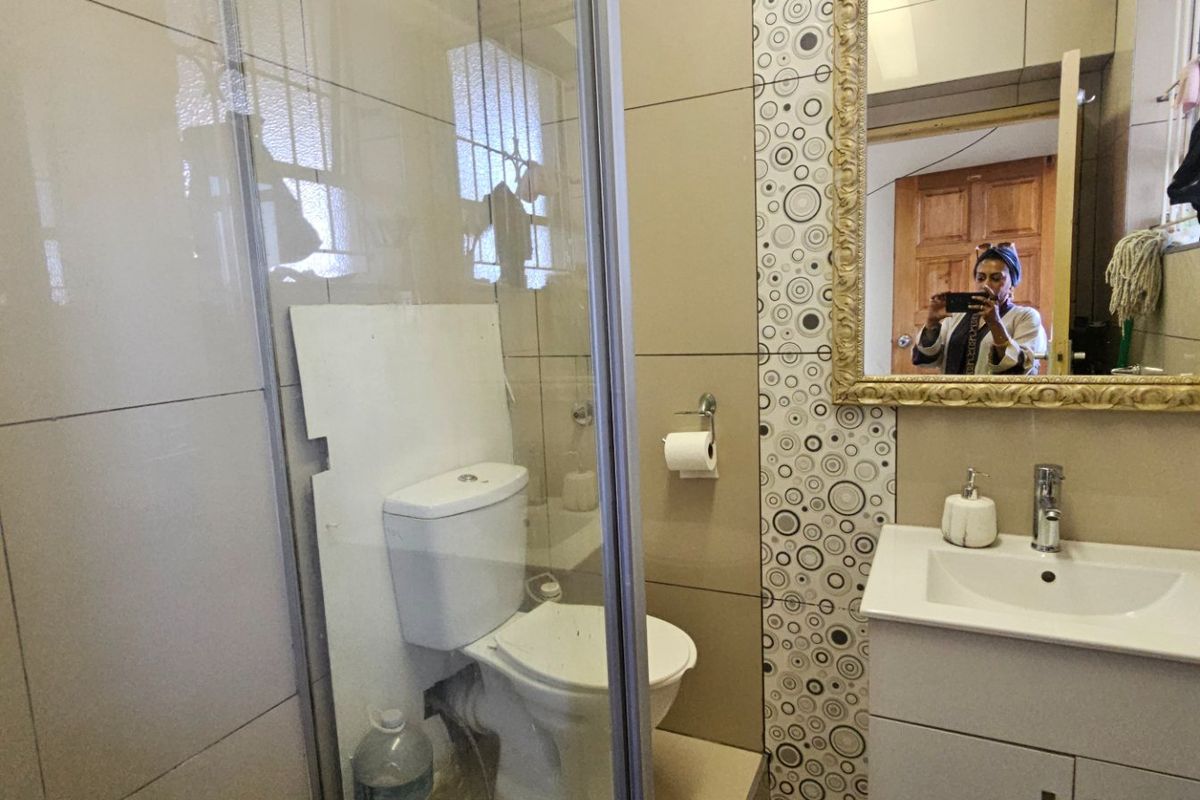 A compact bathroom featuring a shower enclosure, vanity basin, and toilet with visible plumbing and dated wall tiling.