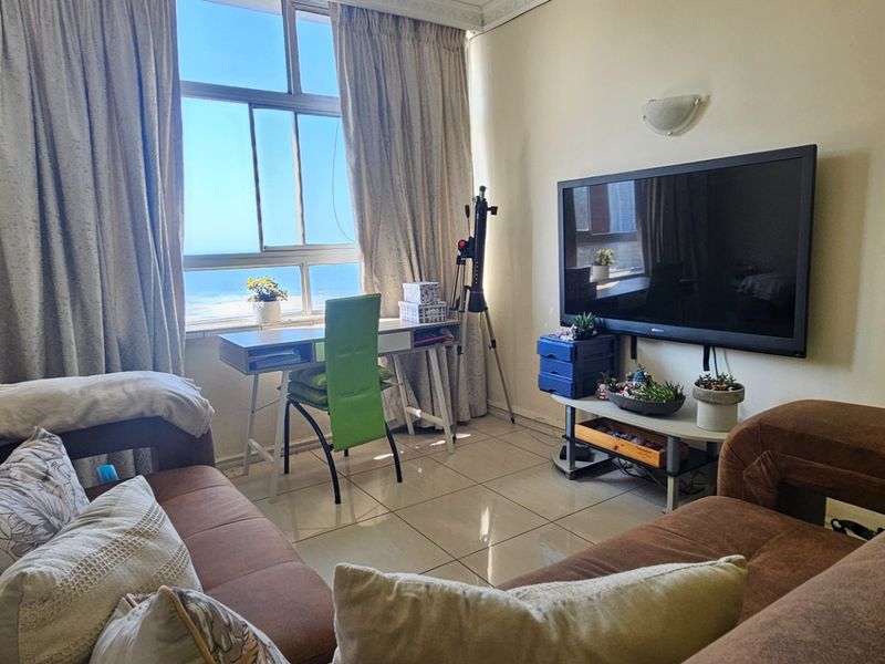 A living room featuring tiled flooring and a large window with natural light, offering a functional space for relaxation and home office use.