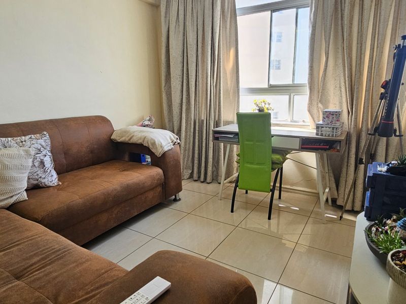 A functional living room featuring tiled flooring and a large window with curtain tracks, providing natural light to the space.