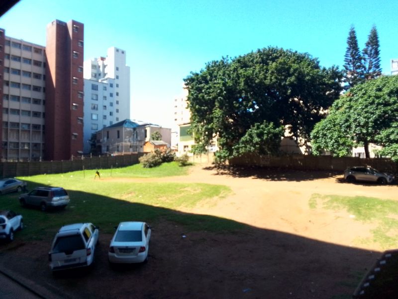 An elevated view overlooking a shared outdoor space with surrounding apartment buildings and mature trees.