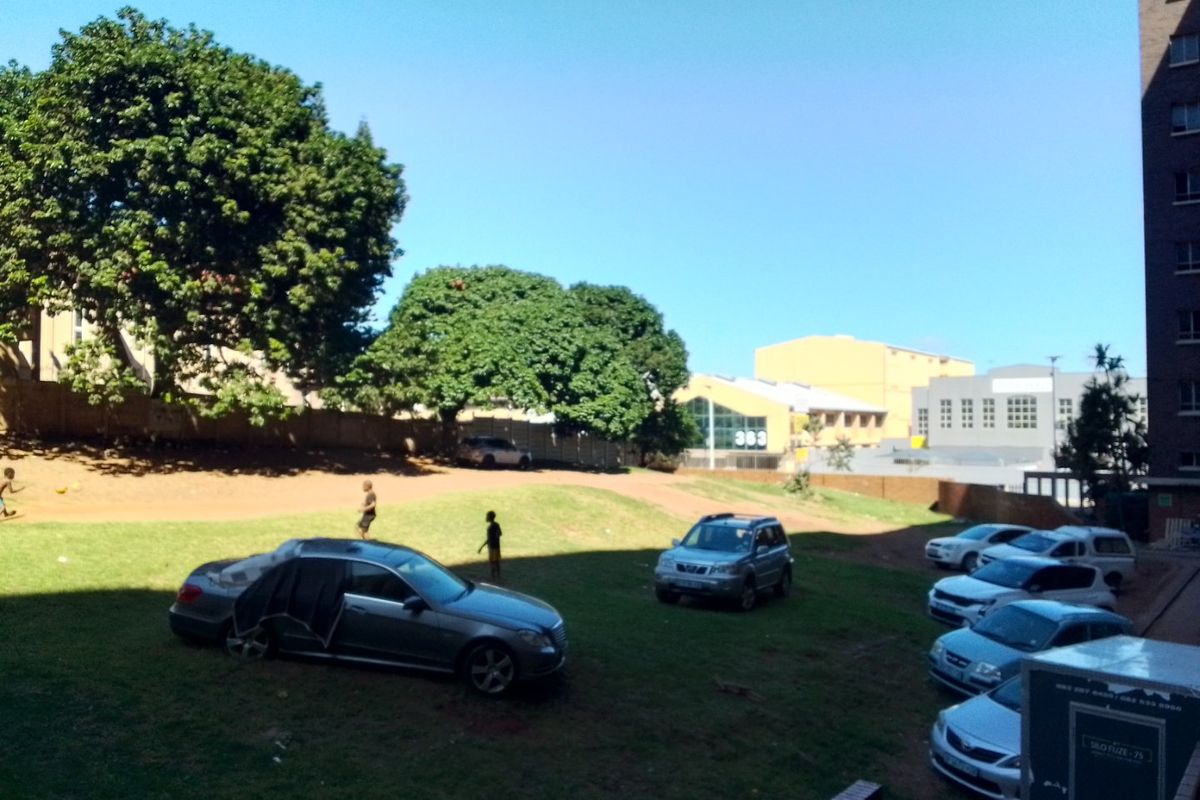 An outdoor communal garden area featuring a grass lawn and boundary wall, viewed from an elevated position.