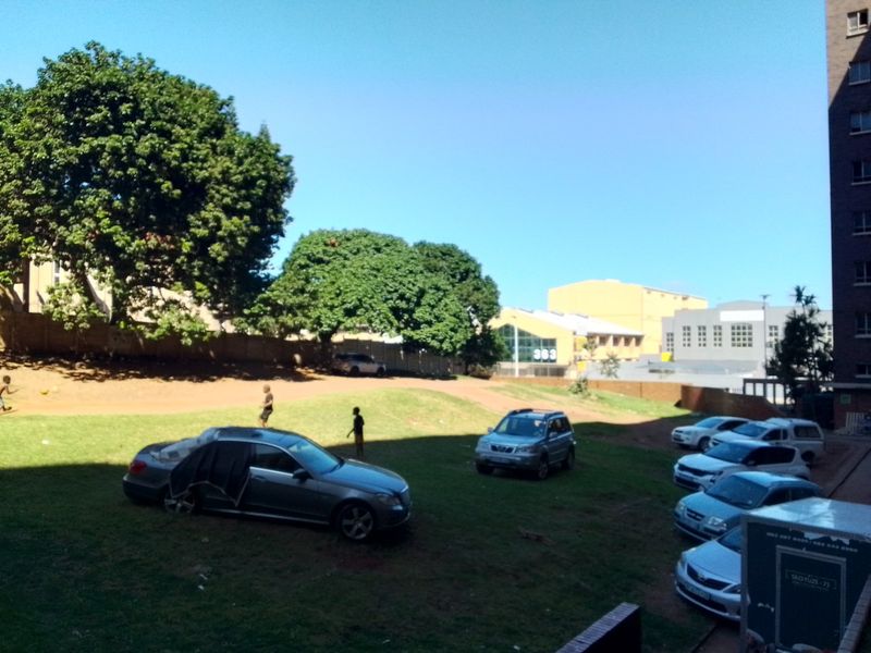 An outdoor communal garden area featuring a grass lawn and boundary wall, viewed from an elevated position.