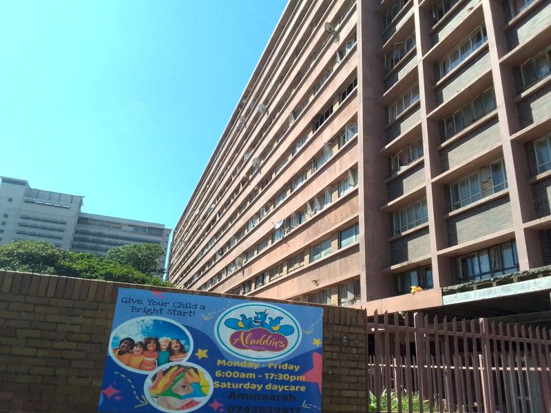 Exterior view of a multi-story apartment building featuring a brick facade and perimeter security fencing.
