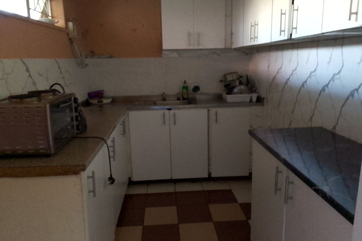 A compact kitchen featuring white built-in cabinetry, dark countertops, tiled backsplash, and a checkered floor pattern, requiring cosmetic updates.