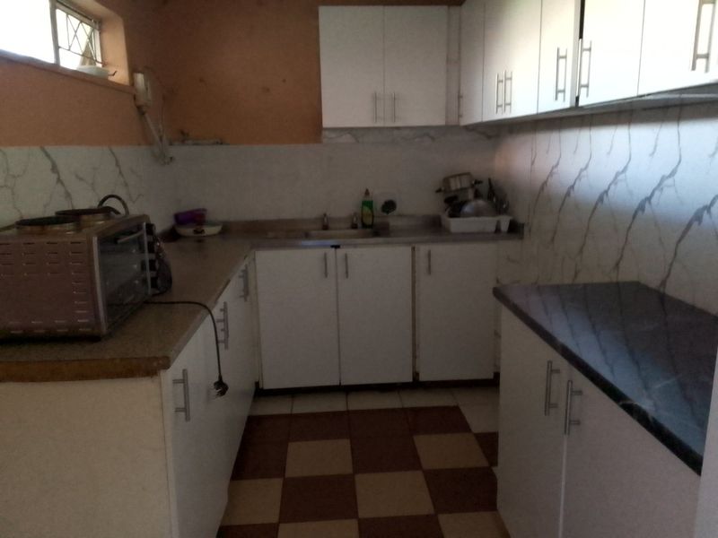 A compact kitchen featuring white built-in cabinetry, dark countertops, tiled backsplash, and a checkered floor pattern, requiring cosmetic updates.