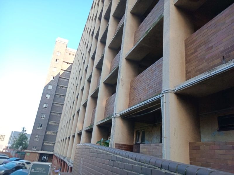 A low-angle exterior view of a multi-story apartment building featuring a repetitive brick and concrete facade with open balcony access.