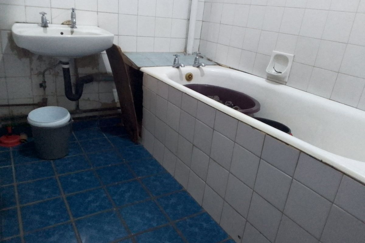A dated bathroom featuring a wall-mounted basin and a built-in bathtub with tiled surrounds, requiring renovation and cosmetic updates to improve functionality and aesthetics.