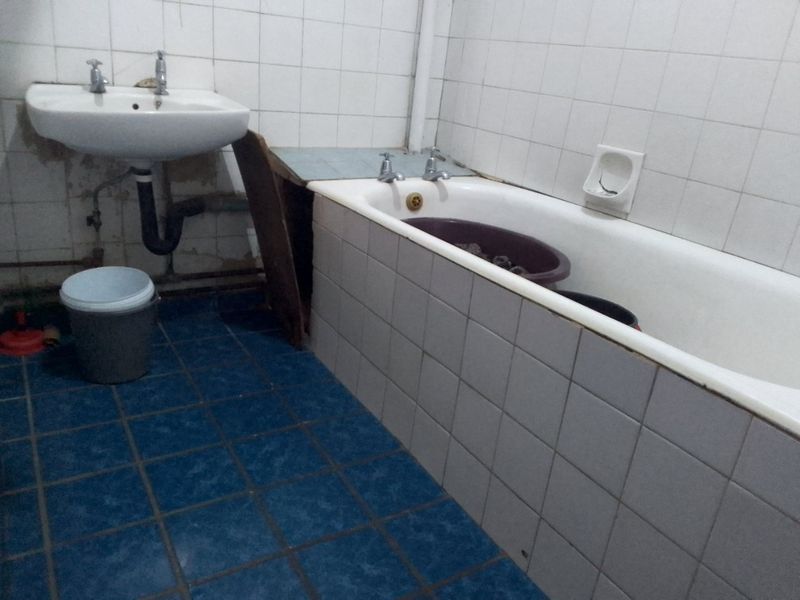 A dated bathroom featuring a wall-mounted basin and a built-in bathtub with tiled surrounds, requiring renovation and cosmetic updates to improve functionality and aesthetics.