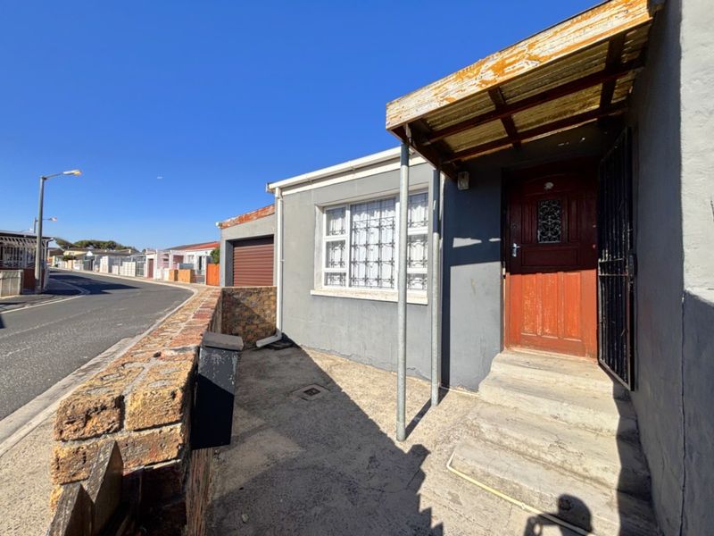 Front entrance of the house featuring a timber door, security gate, and a small concrete porch area with a weathered metal awning.