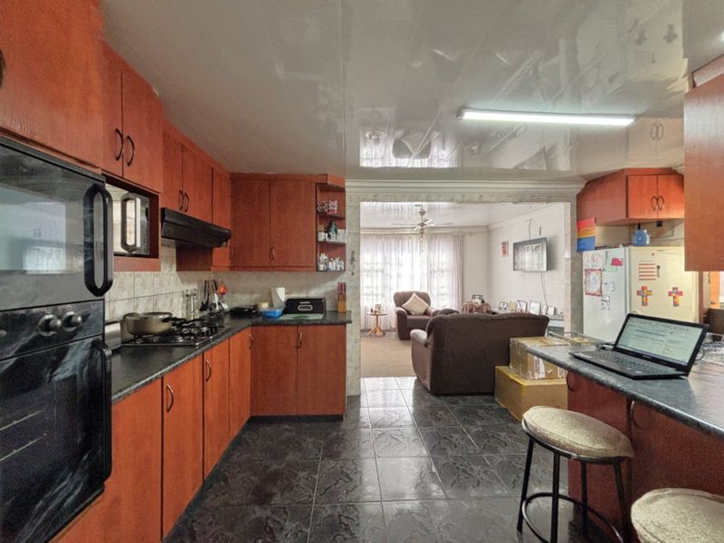 Open-plan kitchen and living area featuring wooden cabinetry, gas hob, built-in oven, and tiled flooring, flowing into a connected lounge space.