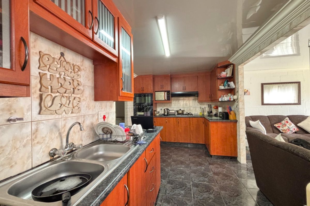 A functional kitchen featuring wooden cabinetry, laminate countertops, a double bowl sink, and built-in appliances, with an open-plan layout connecting to the living area.