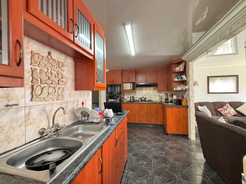 A functional kitchen featuring wooden cabinetry, laminate countertops, a double bowl sink, and built-in appliances, with an open-plan layout connecting to the living area.