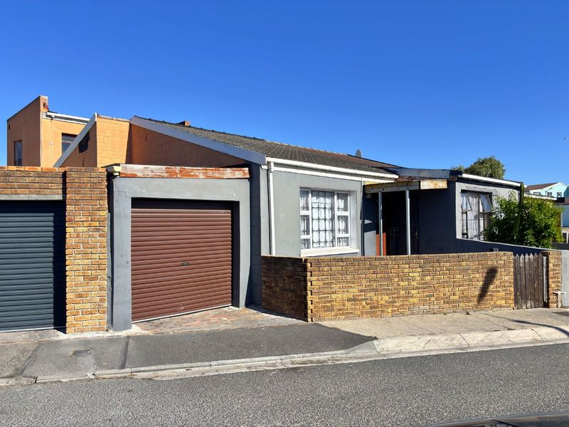 Front elevation of a single-story house featuring a roller garage door, brick boundary wall, and security-barred windows.