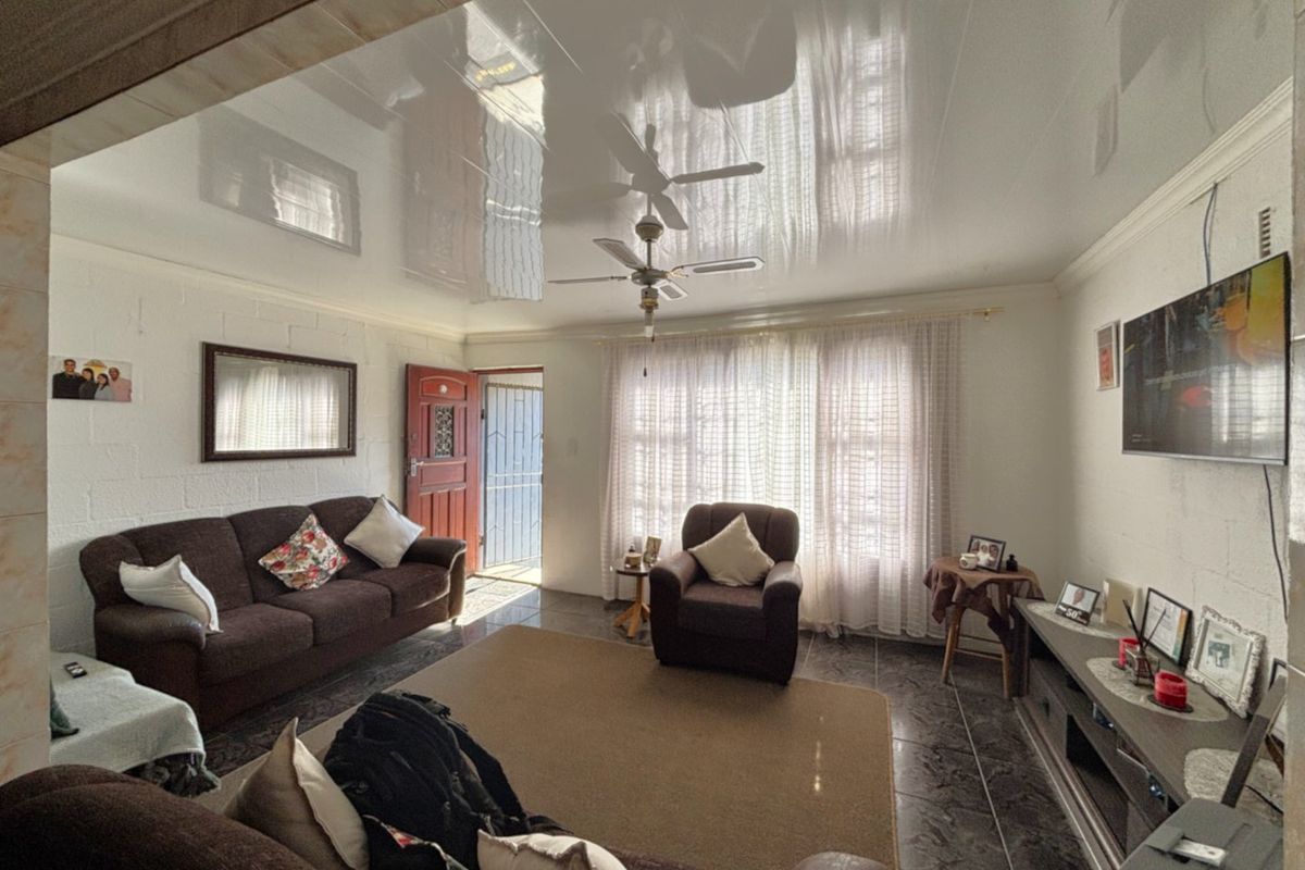 A living room featuring a glossy stretch ceiling, ceiling fan, and tiled flooring, with direct access to an exterior security gate.