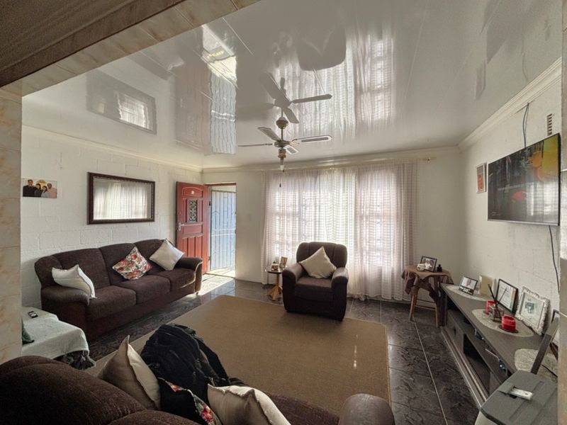 A living room featuring a glossy stretch ceiling, ceiling fan, and tiled flooring, with direct access to an exterior security gate.
