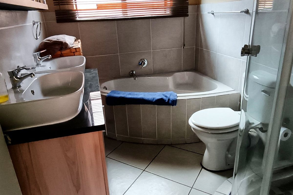 A functional bathroom featuring a double vanity, built-in bathtub, separate shower enclosure, and tiled finishes throughout.