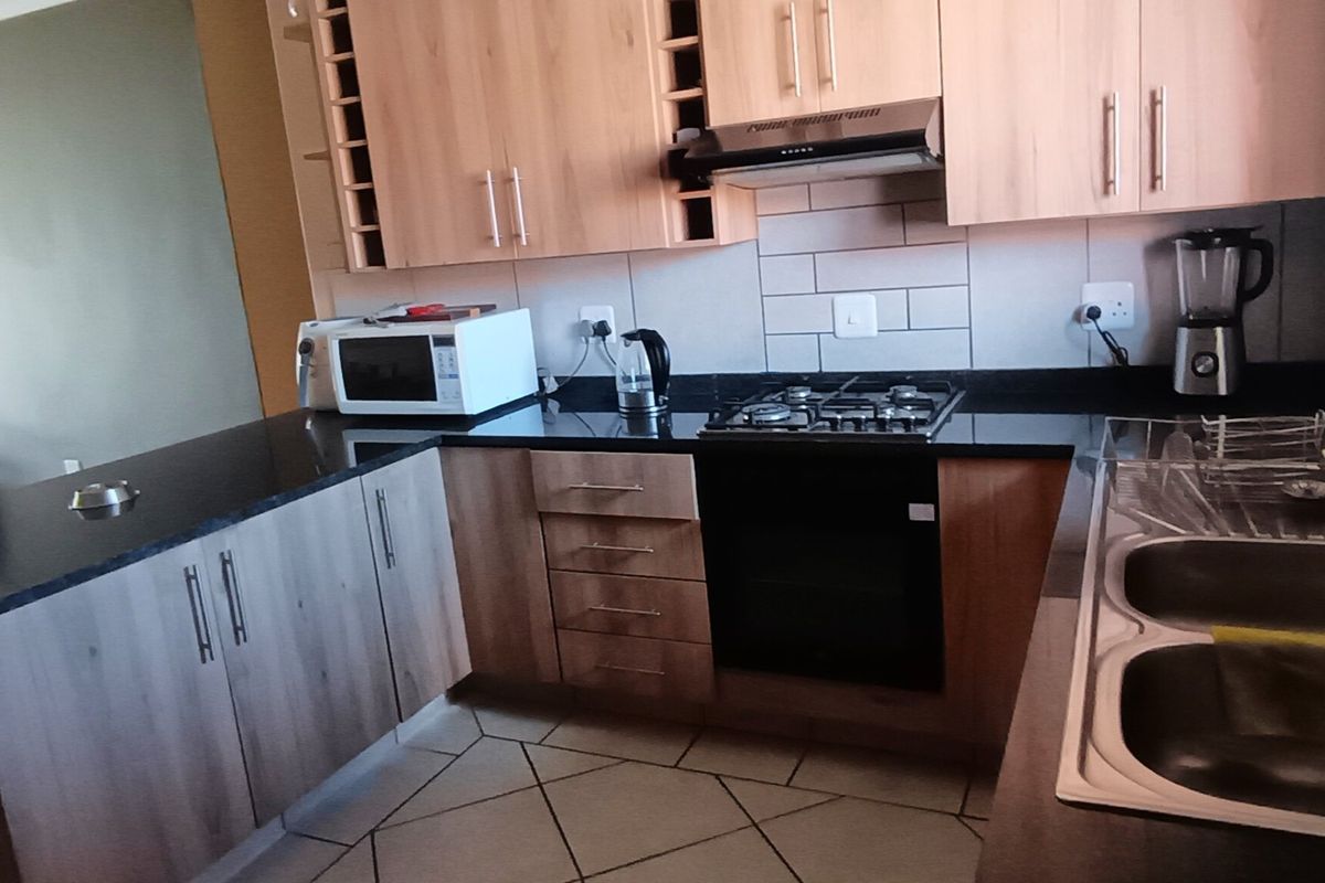 Modern kitchen featuring light wood cabinetry, dark granite countertops, a gas hob with extractor, and a double stainless steel sink.