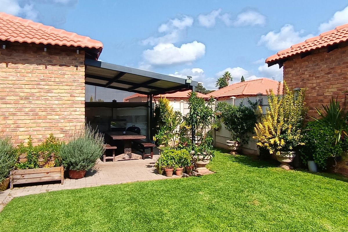 A well-maintained outdoor living area featuring a covered patio with brick construction and a landscaped garden space.