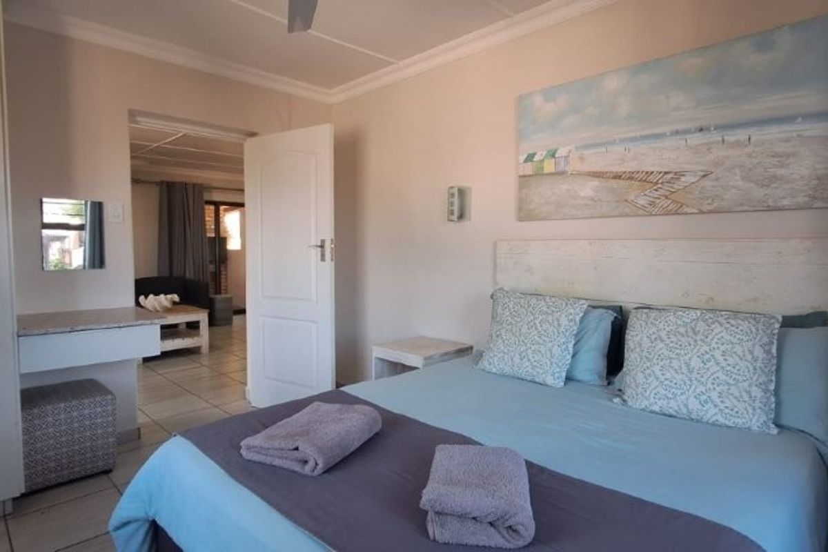 A well-lit bedroom featuring built-in cupboards, tiled flooring, and a doorway leading to an adjacent living area.