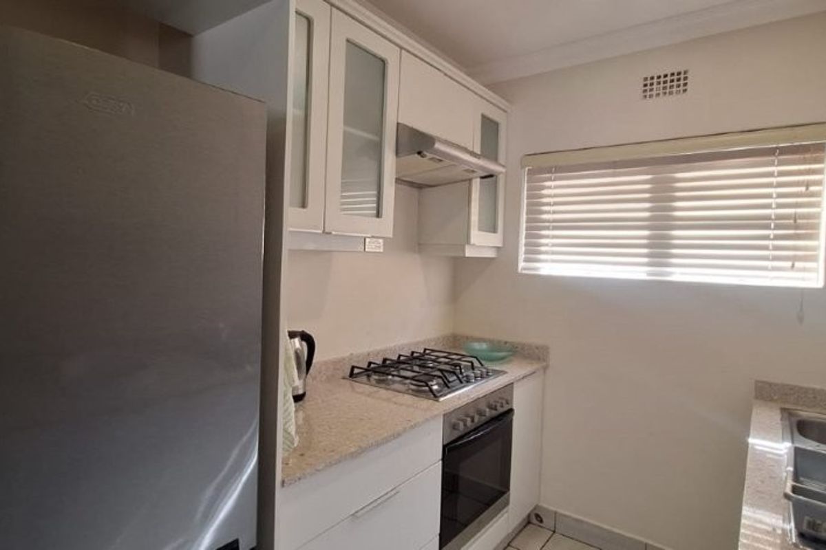 A functional kitchen featuring white cabinetry, stone countertops, a built-in gas hob, oven, extractor fan, and a stainless steel sink.
