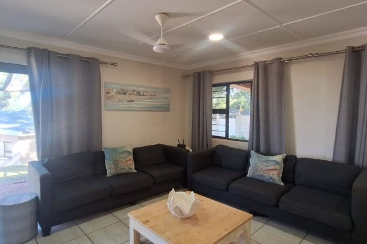 A bright living room featuring tiled flooring, large sliding glass doors providing outdoor access, and a ceiling fan.