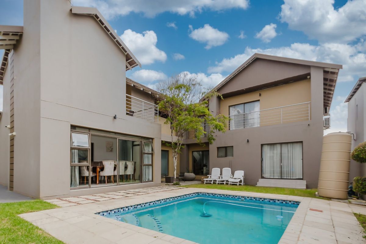 Rear view of a multi-story house featuring a swimming pool, paved patio area, and upper-level balconies.