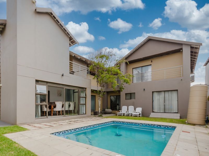 Rear view of a multi-story house featuring a swimming pool, paved patio area, and upper-level balconies.