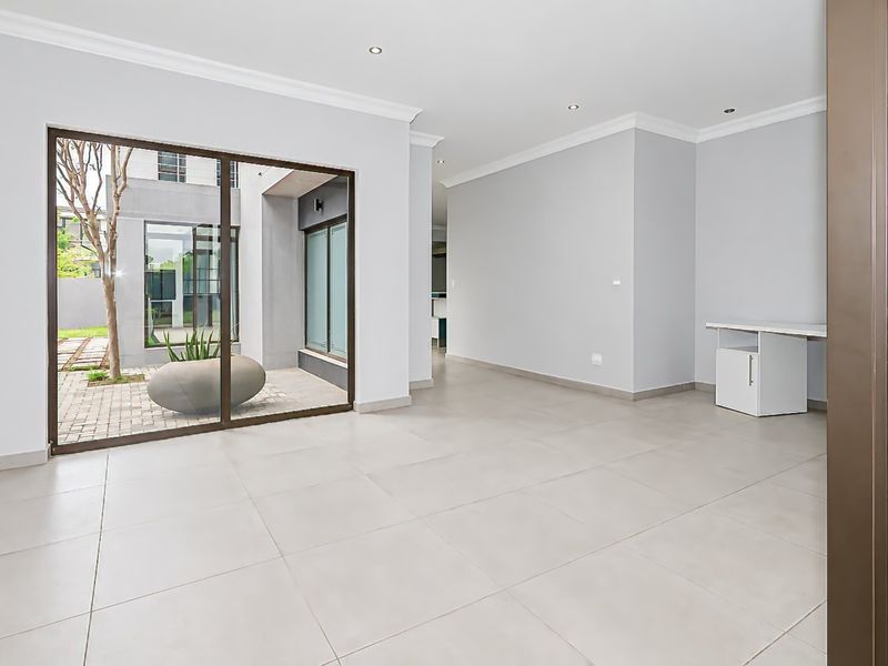 A bright, open-plan living area featuring neutral tiled flooring, recessed lighting, and a large sliding glass door providing access to an outdoor courtyard.