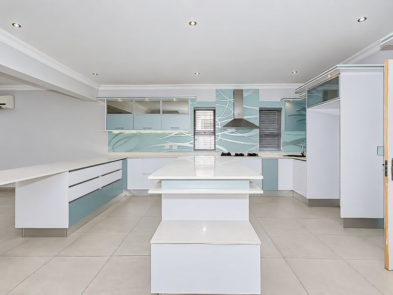 Modern kitchen featuring a central island, quartz countertops, sleek cabinetry, and integrated extractor fan, offering a clean and functional culinary space.