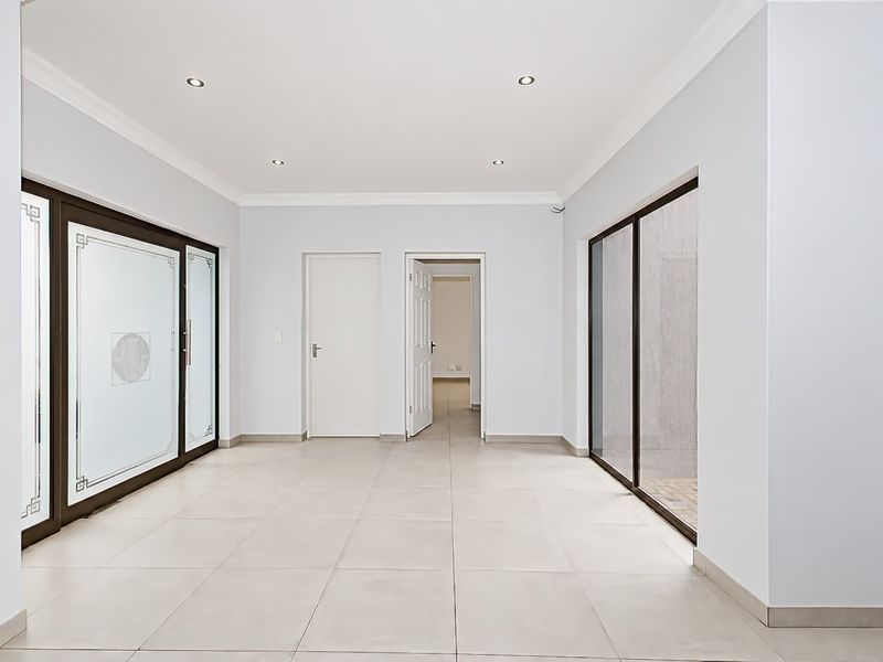 A bright, open-plan living area featuring neutral tiled flooring, recessed downlights, and large sliding glass doors providing access to the exterior.