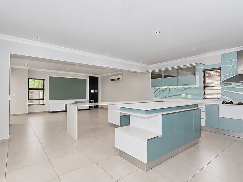 Spacious open-plan living and kitchen area featuring a modern island, built-in cabinetry, gas hob, and neutral tiled flooring throughout.