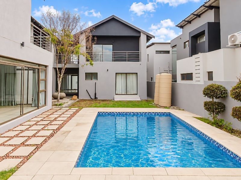 Rear exterior view featuring a modern swimming pool, paved deck, and multi-level residential structure with balconies and sliding glass doors.