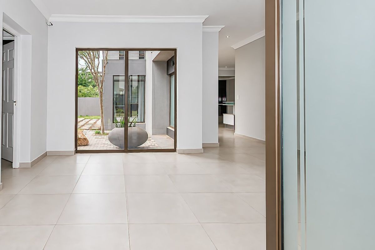 A bright, open-plan living area featuring neutral tiled flooring, modern recessed lighting, and large sliding glass doors providing access to the exterior courtyard.