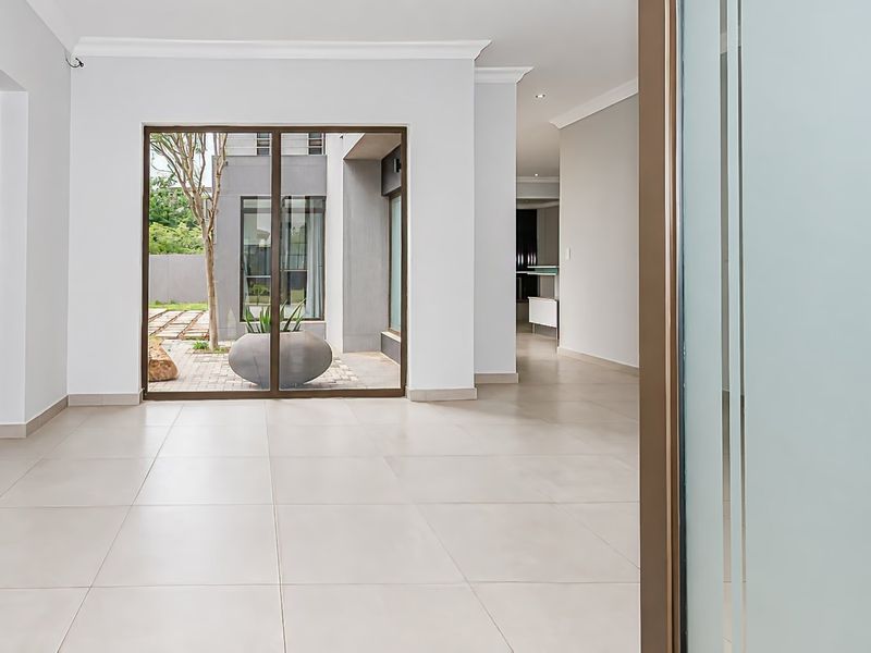 A bright, open-plan living area featuring neutral tiled flooring, modern recessed lighting, and large sliding glass doors providing access to the exterior courtyard.