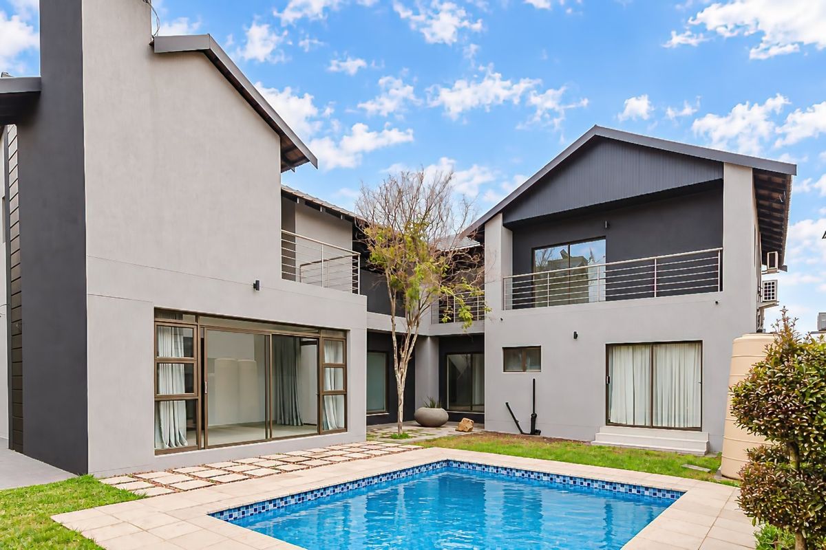 Rear view of a modern two-story house featuring a swimming pool, paved patio area, and upper-level balconies with contemporary architectural finishes.