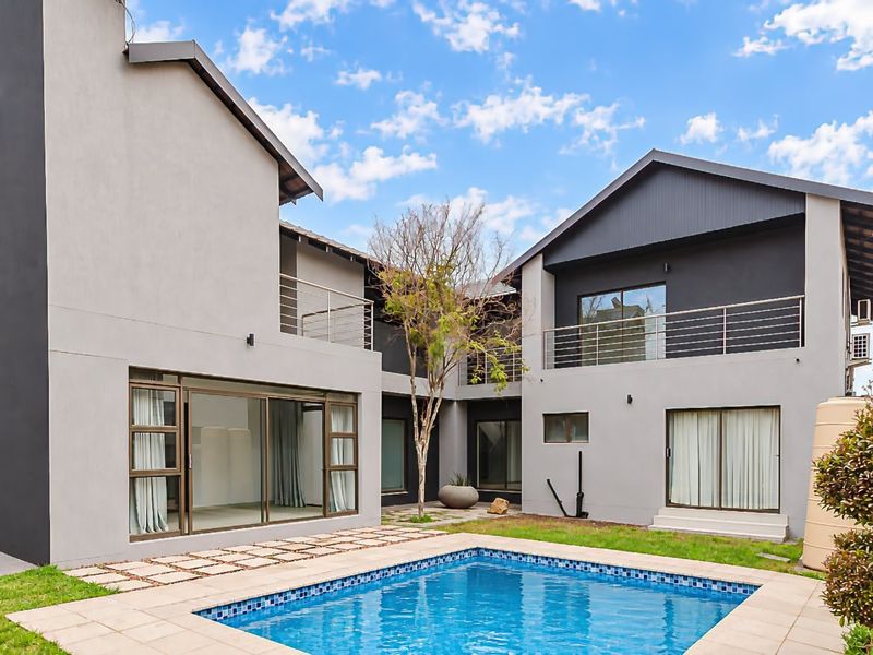 Rear view of a modern two-story house featuring a swimming pool, paved patio area, and upper-level balconies with contemporary architectural finishes.