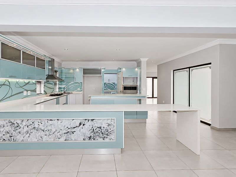 Spacious modern kitchen featuring light blue cabinetry, stone countertops, a large central island, and integrated appliances with neutral tiled flooring.