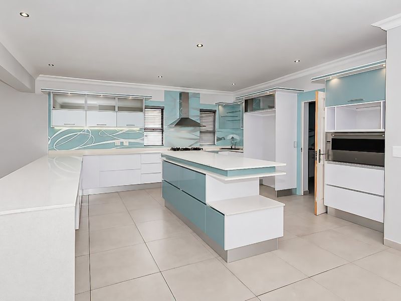 Modern, spacious kitchen featuring a central island, built-in oven, extractor fan, and sleek cabinetry with quartz countertops and tiled flooring.