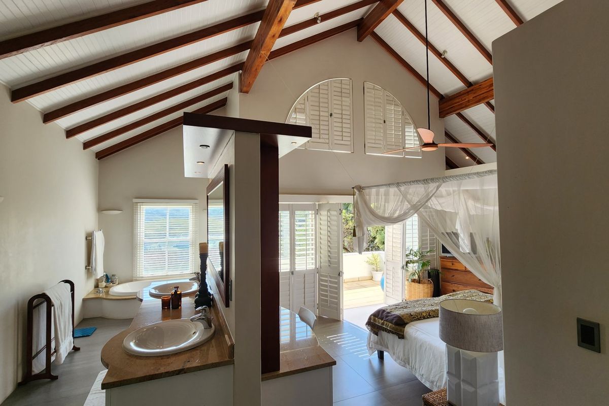 Spacious bedroom featuring a vaulted ceiling with exposed timber beams, an integrated en-suite bathroom with double vanity, and direct access to a private balcony.