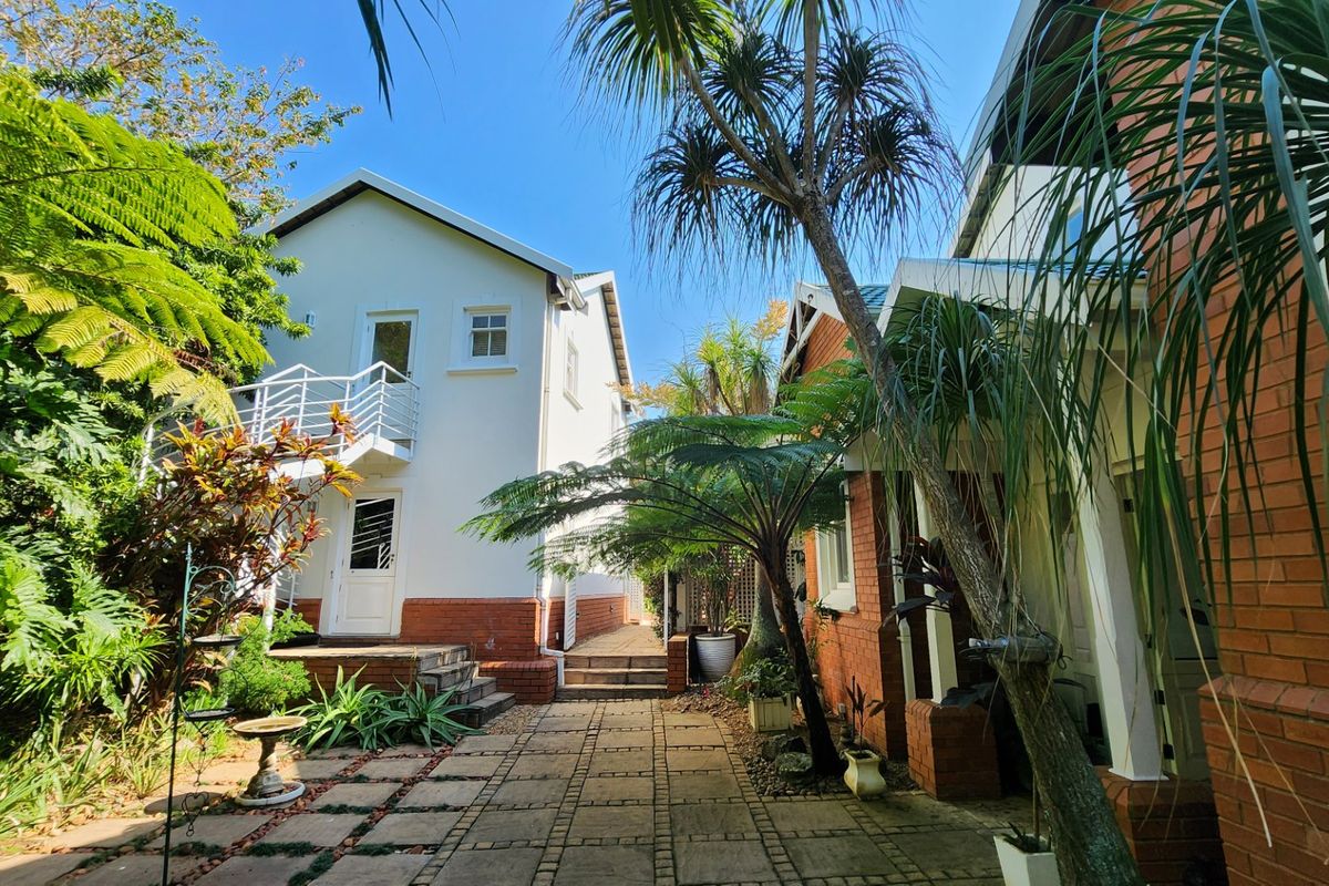 A well-maintained rear courtyard featuring paved pathways, established garden greenery, and an external staircase leading to the upper level of the residence.