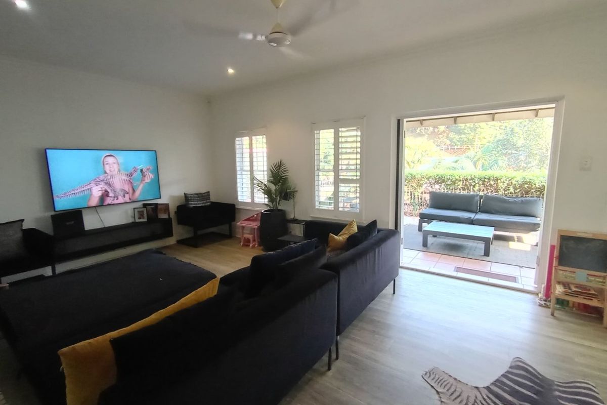 Spacious living room featuring light-toned laminate flooring, recessed lighting, ceiling fan, and plantation shutters, with direct access to an outdoor patio area.