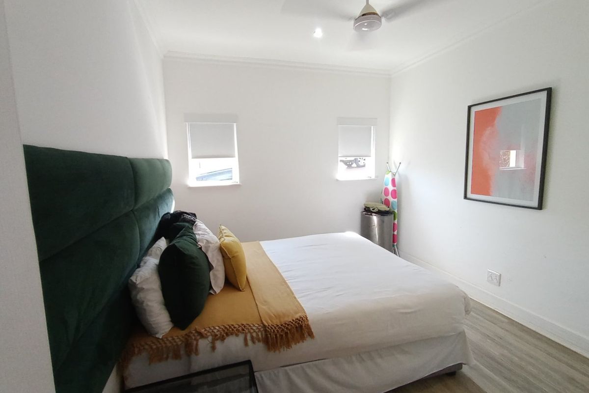 A well-maintained bedroom featuring laminate flooring, a ceiling fan, and dual windows with roller blinds.